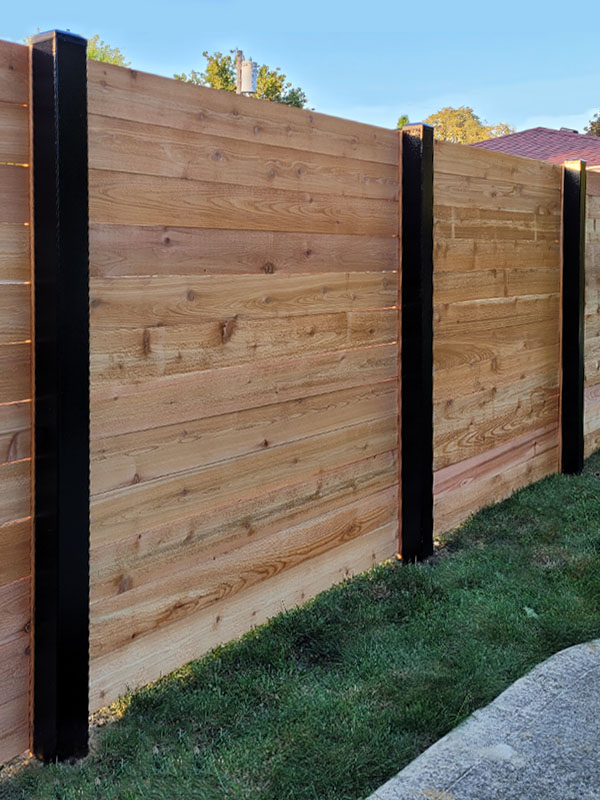 Decorative steel fence with masonry columns and wood arbor over the gate